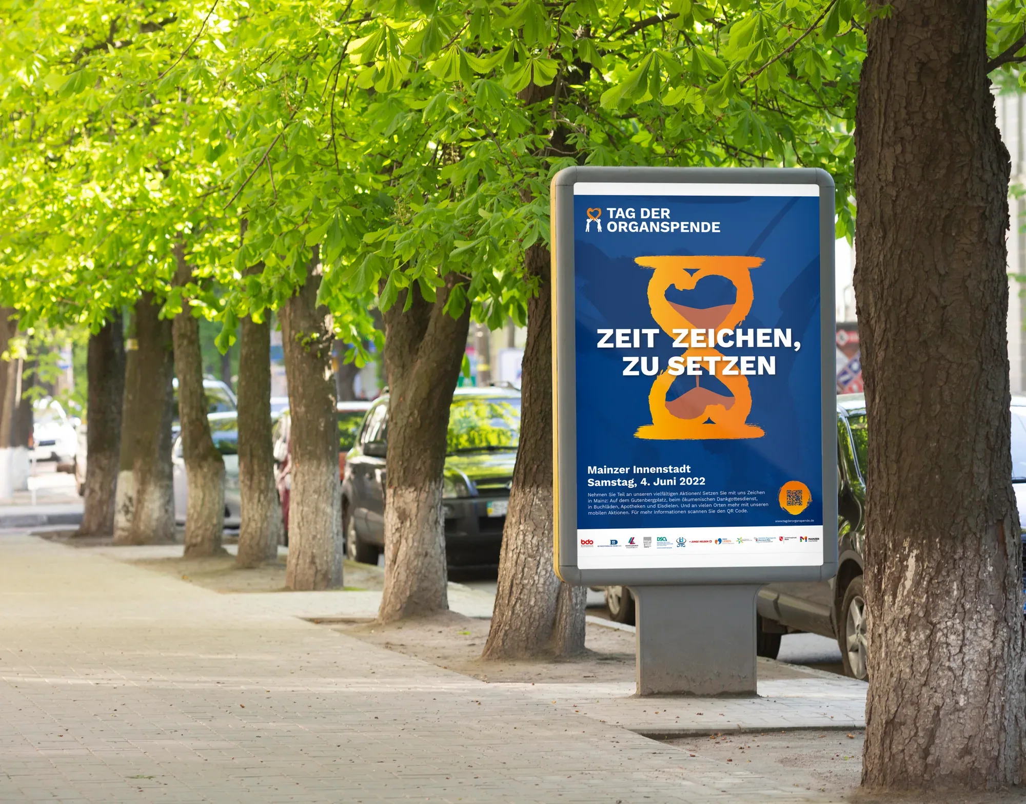Das Citylight-Plakat in der Anwendung im Straßenraum, unter der Baumreihe einer Mainzer Allee.